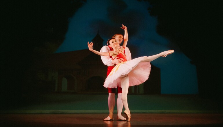 Image of two dancers performing positions in a ballet dance onstage in costume